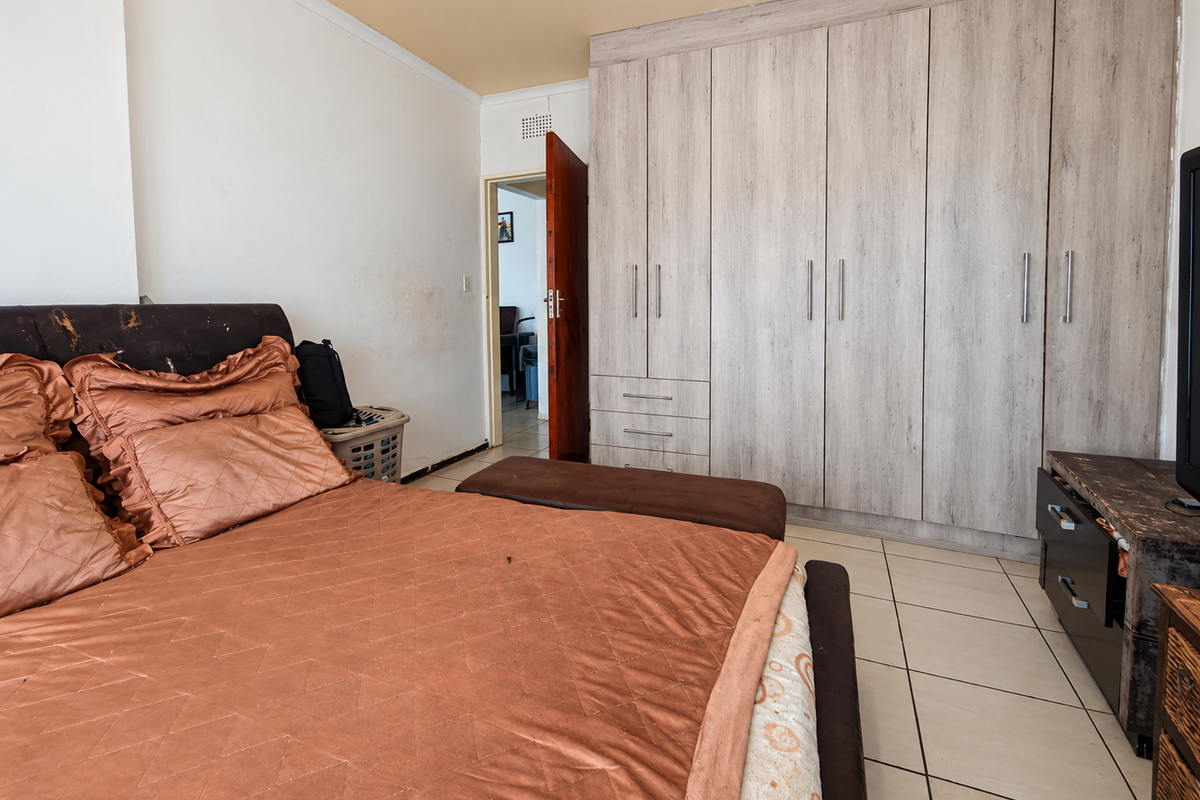 A bedroom featuring light wood-finish built-in cupboards and tiled flooring, with access to an adjacent room through a wooden door.