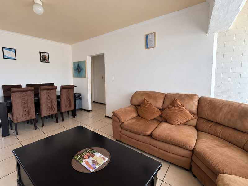 An open-plan living and dining area featuring tiled flooring and a painted brick feature wall, providing a functional and versatile living space.
