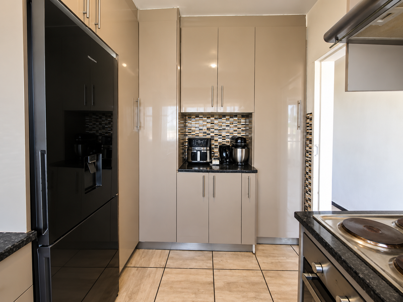 Modern kitchen featuring high-gloss cabinetry, granite countertops, mosaic tile backsplash, and integrated appliances including an oven and hob.