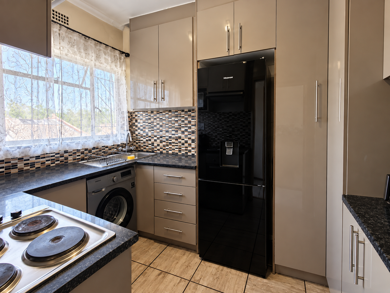 Modern kitchen featuring sleek high-gloss cabinetry, granite countertops, a mosaic tile backsplash, and integrated appliances including a hob and washing machine.