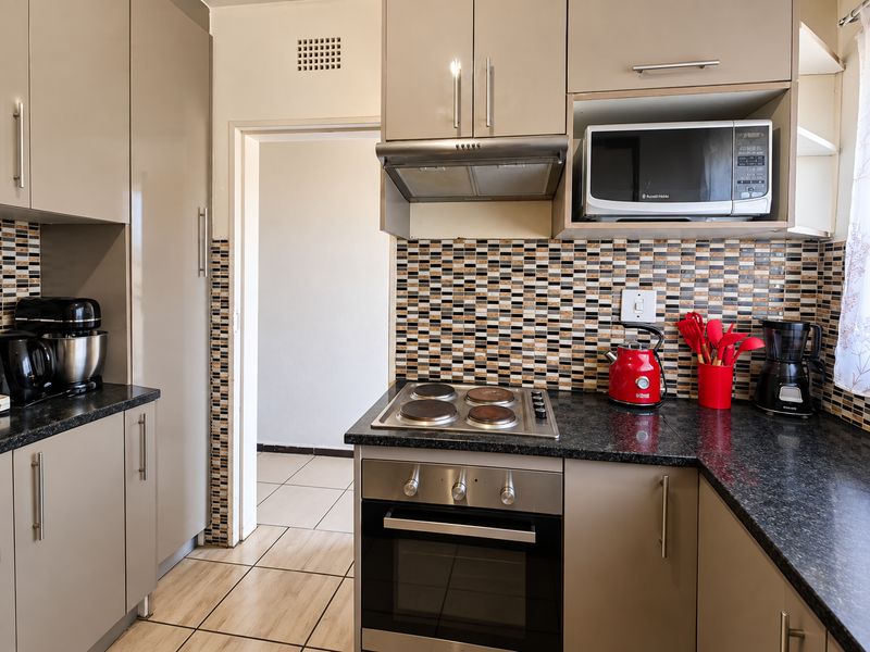 A functional kitchen featuring modern taupe cabinetry, dark granite-look countertops, a mosaic tile backsplash, and integrated appliances including an oven and hob.