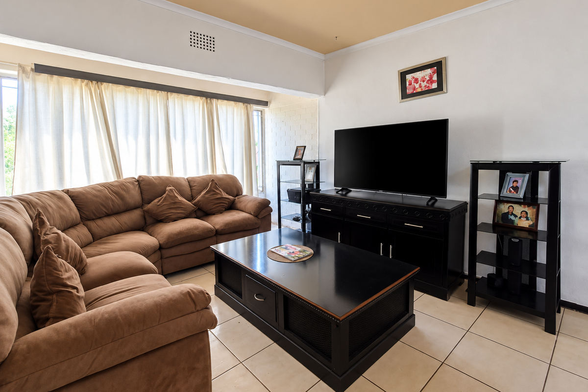 A comfortable living room featuring ceramic floor tiles, a neutral color palette, and a recessed ceiling detail, providing a functional and well-lit space.