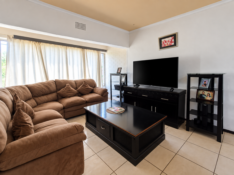 A comfortable living room featuring ceramic floor tiles, a neutral color palette, and a recessed ceiling detail, providing a functional and well-lit space.