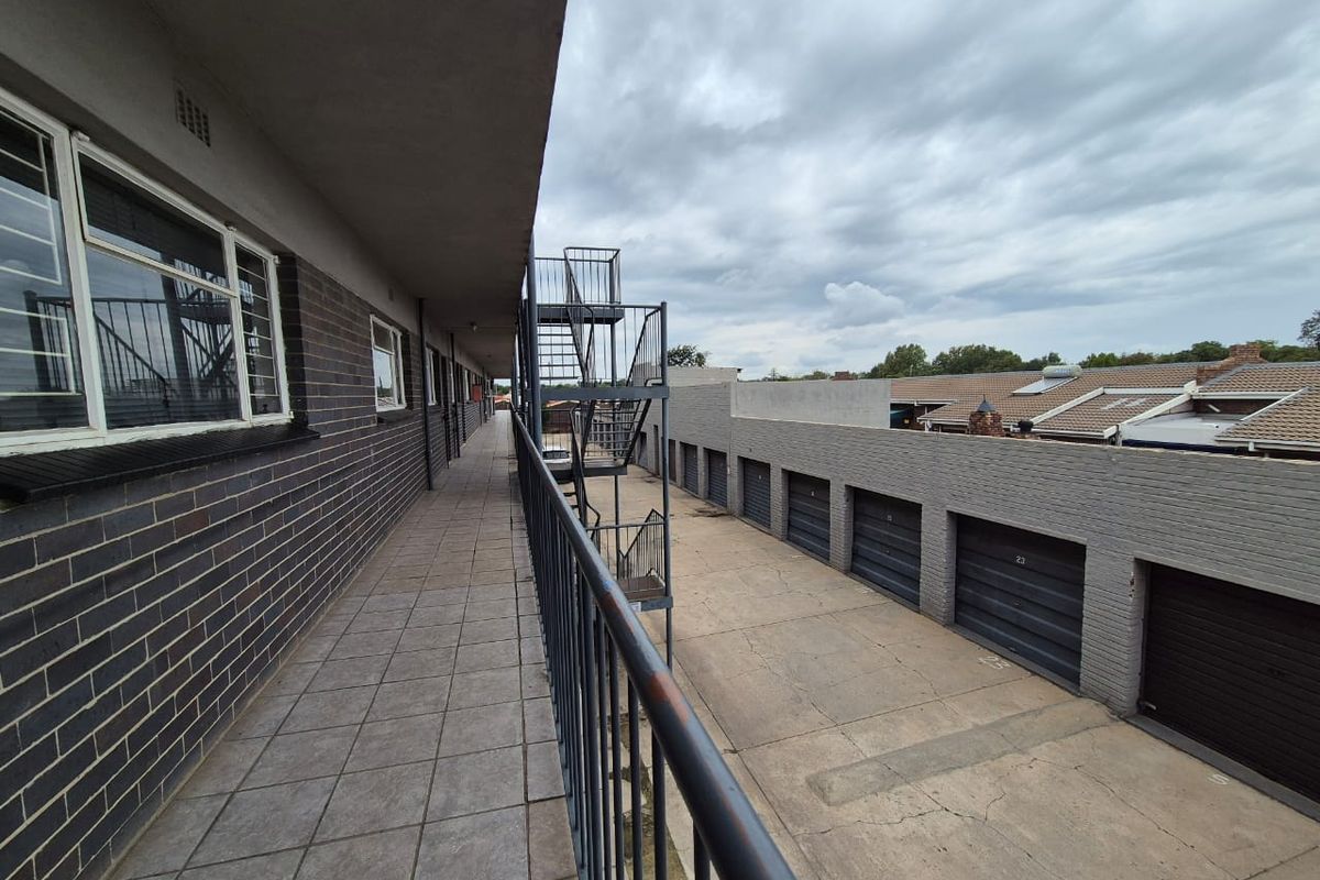 Exterior view of a flat complex featuring a tiled walkway, metal fire escape staircase, and a row of garages below.