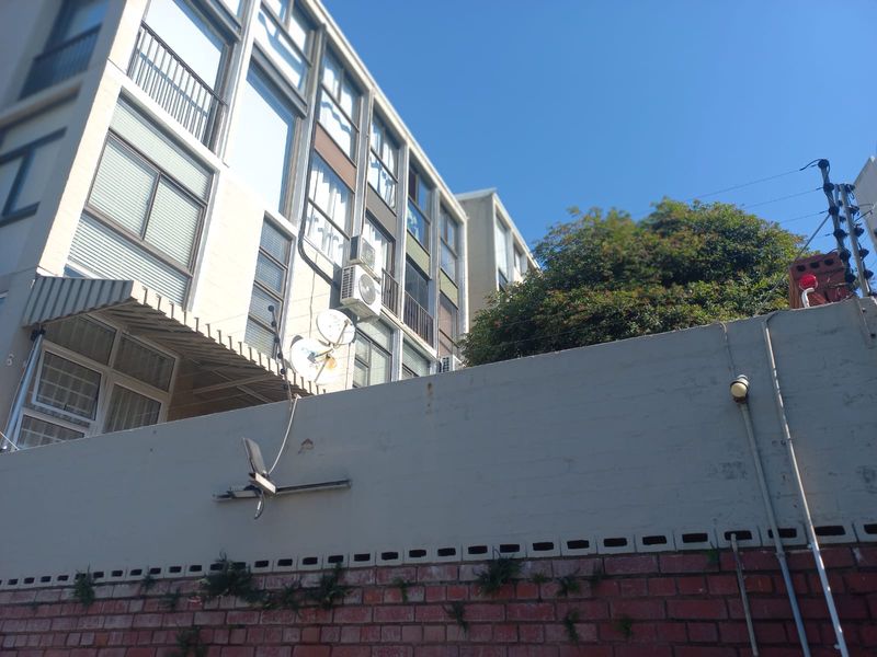 View of the rear facade of the apartment building featuring brick boundary walling, electric fencing, and mounted air conditioning units.