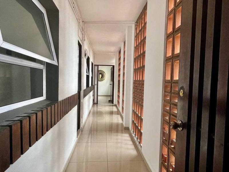 A well-lit hallway featuring tiled flooring, decorative breeze block wall detailing, and timber slat accents, providing a clean and modern transition between rooms.