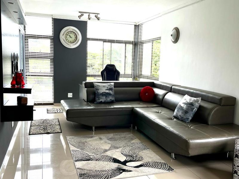 A modern living room featuring large format floor tiles, neutral walls with a dark accent wall, and extensive window coverage with venetian blinds.