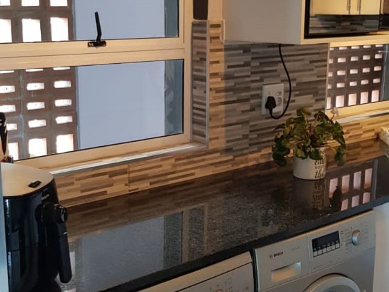 A well-maintained kitchen featuring granite countertops, a tiled backsplash, and integrated appliances including a dishwasher and washing machine.