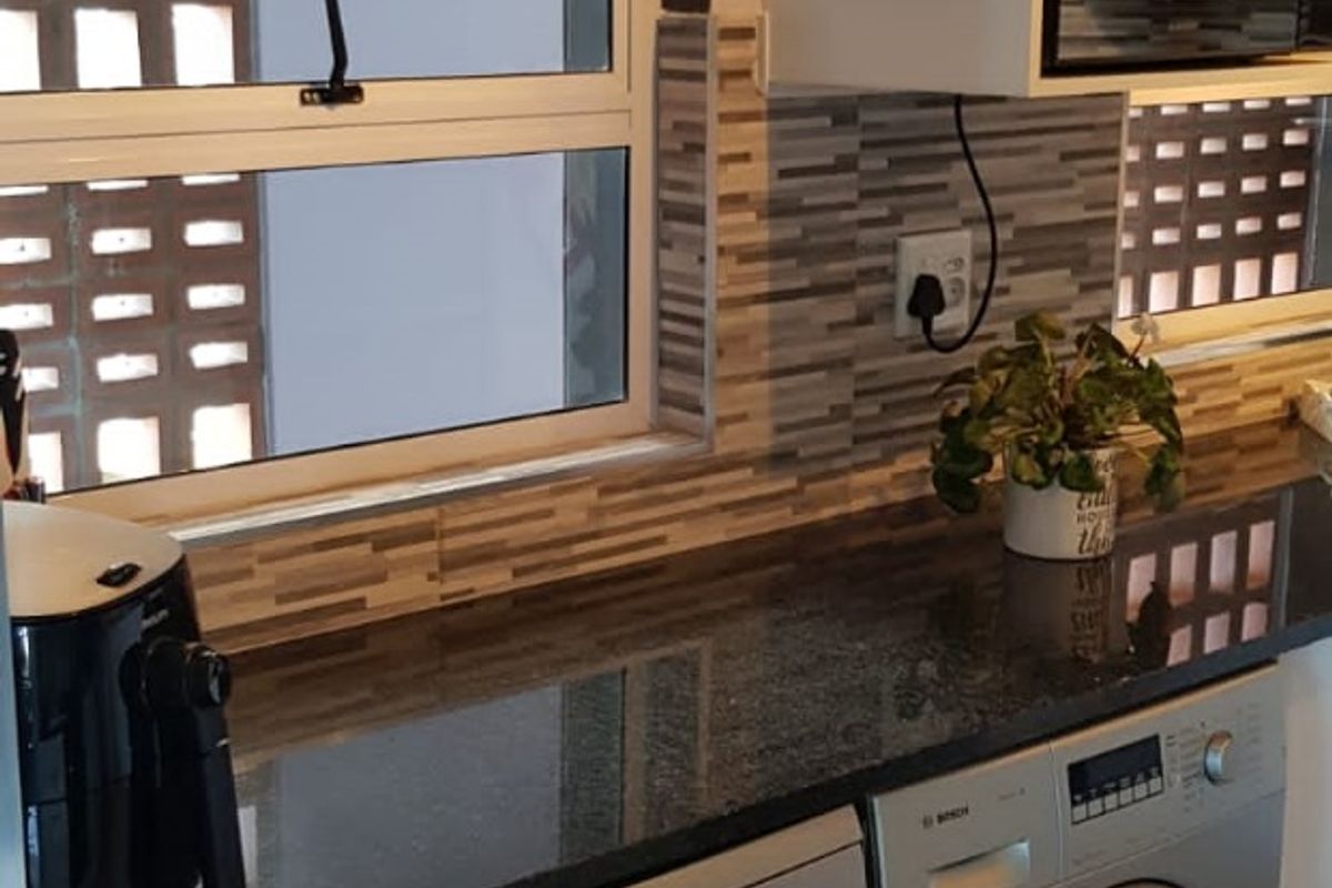 A well-maintained kitchen featuring granite countertops, a tiled backsplash, and integrated appliances including a dishwasher and washing machine.