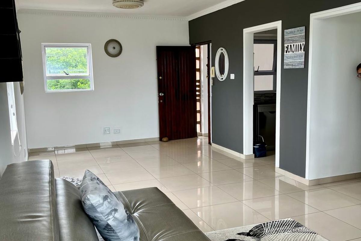 Spacious living area featuring neutral tiled flooring, decorative ceiling cornicing, and a dark feature wall, providing a clean and well-maintained foundation for living.