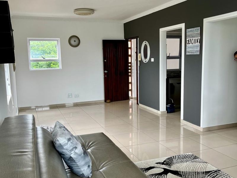 Spacious living area featuring neutral tiled flooring, decorative ceiling cornicing, and a dark feature wall, providing a clean and well-maintained foundation for living.