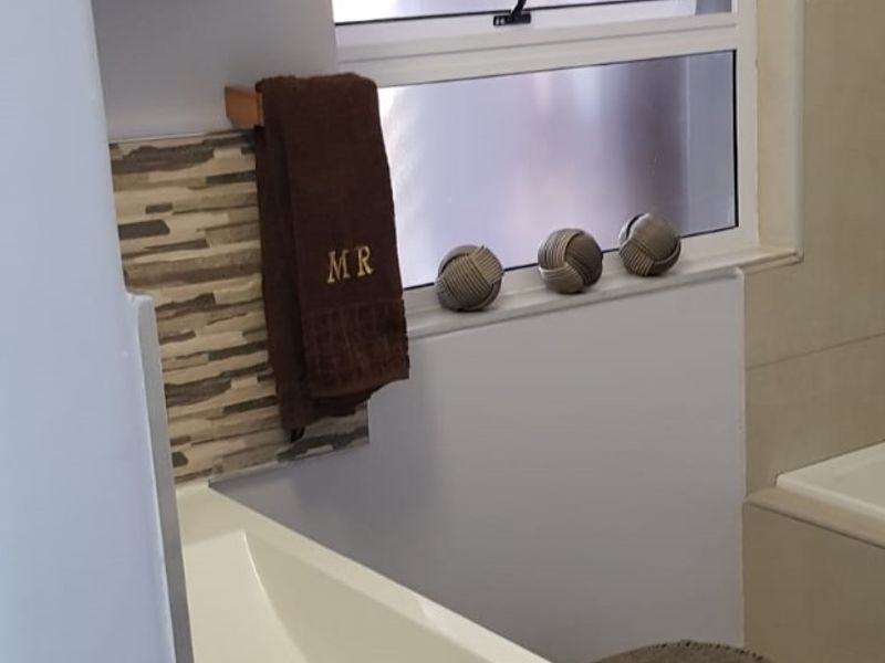 A modern bathroom featuring a vanity with an integrated basin, tiled splashback, and a built-in bathtub with neutral wall and floor tiles.