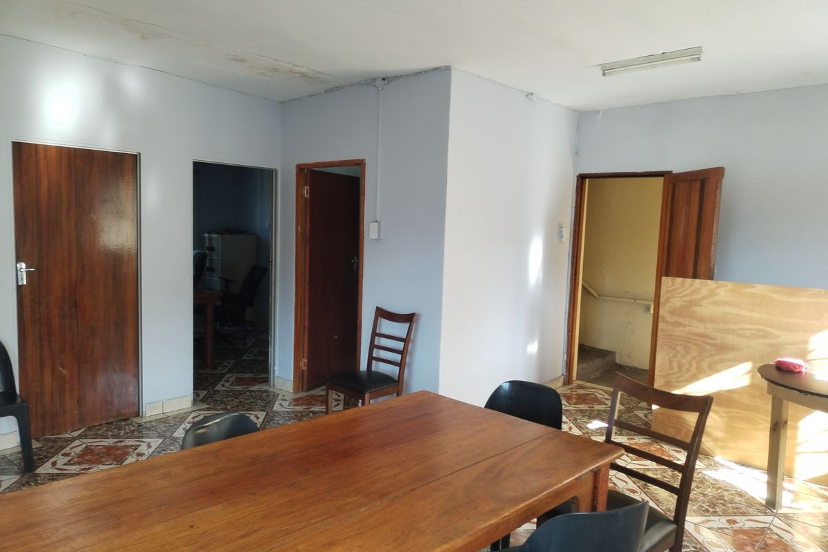A multi-room interior space featuring patterned floor tiles, multiple wooden doors, and visible ceiling damage, offering a functional layout for renovation.