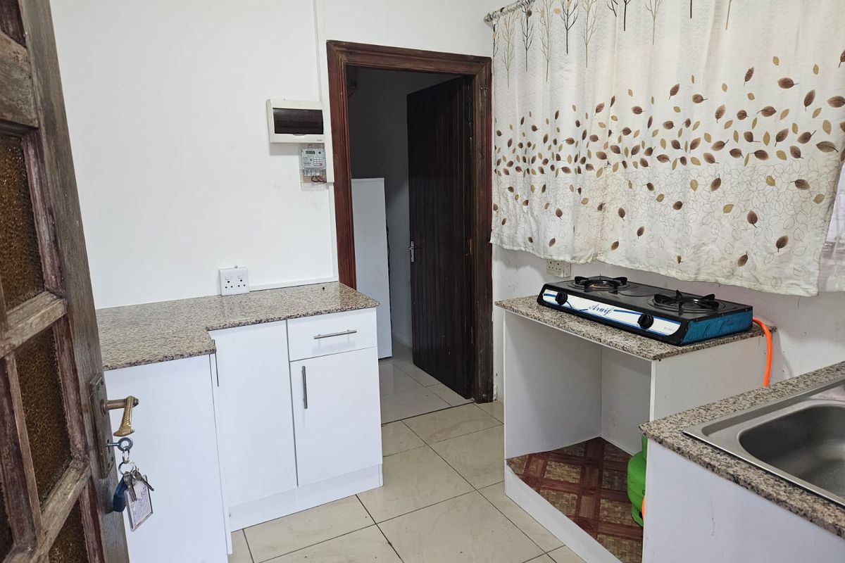 A functional kitchen featuring granite countertops, built-in white cabinetry, a gas hob, and tiled flooring, offering a practical layout for daily meal preparation.