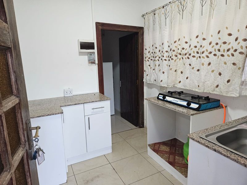 A functional kitchen featuring granite countertops, built-in white cabinetry, a gas hob, and tiled flooring, offering a practical layout for daily meal preparation.