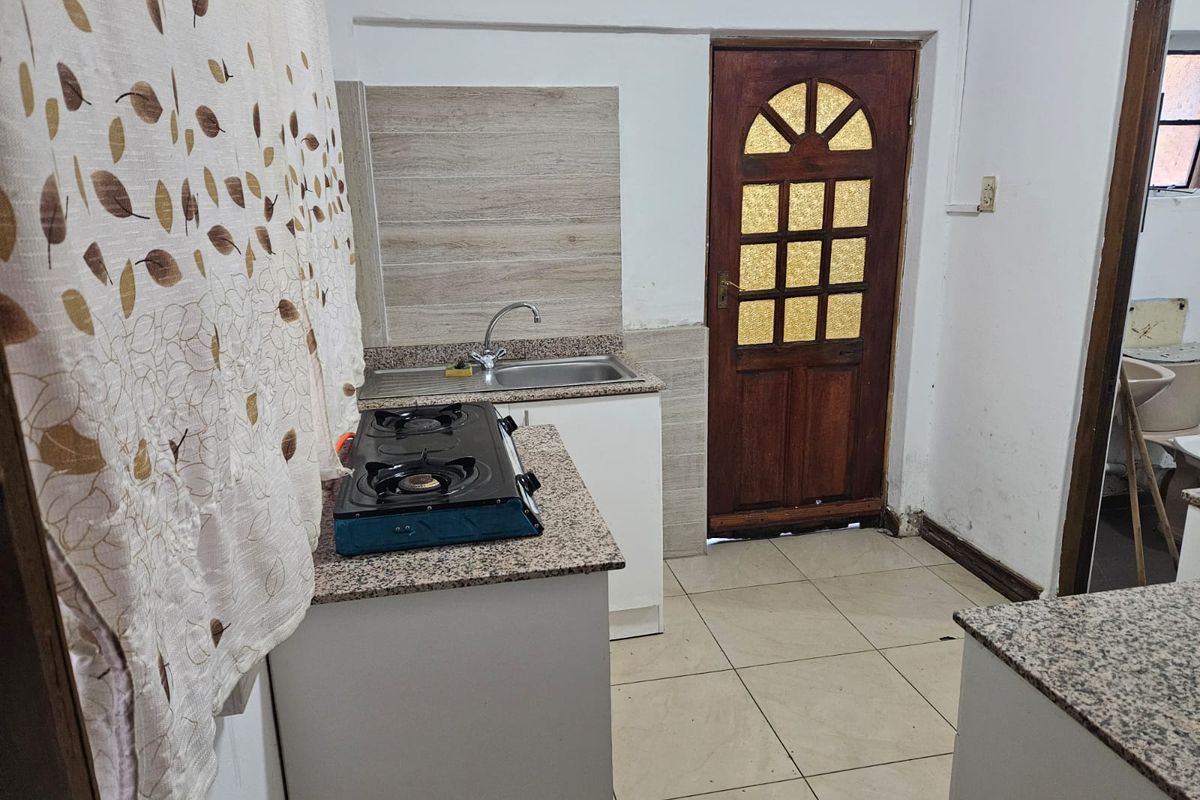Compact kitchen featuring granite countertops, stainless steel sink, tiled splashback, and direct access to an exterior door.