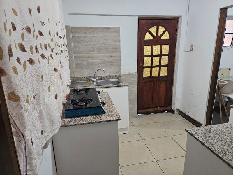 Compact kitchen featuring granite countertops, stainless steel sink, tiled splashback, and direct access to an exterior door.