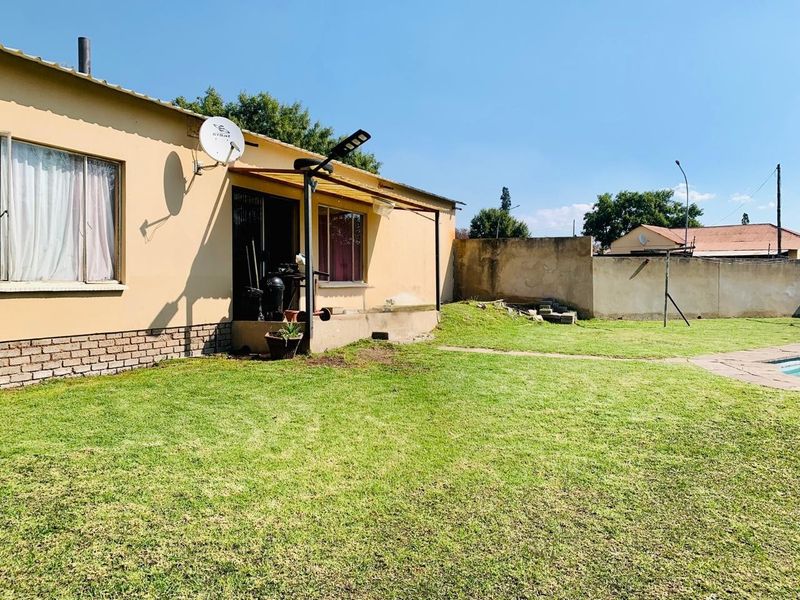 Rear view of the property featuring a lawn, concrete patio area, and perimeter boundary wall.
