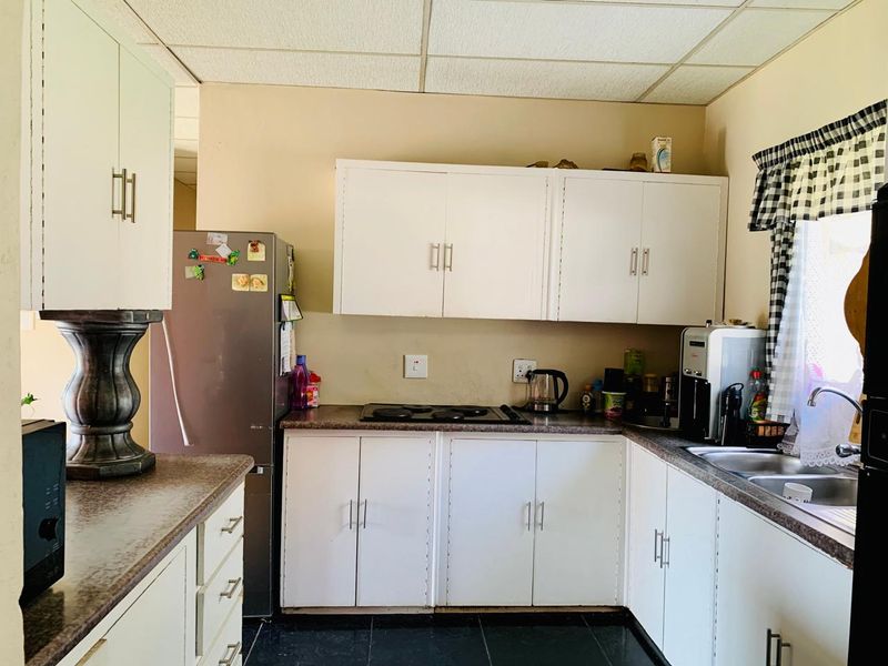 A functional kitchen featuring white cabinetry, laminate countertops, an electric hob, and a double basin sink, offering potential for modern updates.