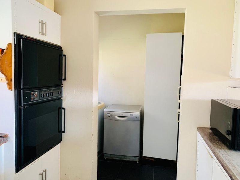 A functional scullery area featuring a built-in double oven, laminate countertops, and direct access to a utility space with tiled flooring.