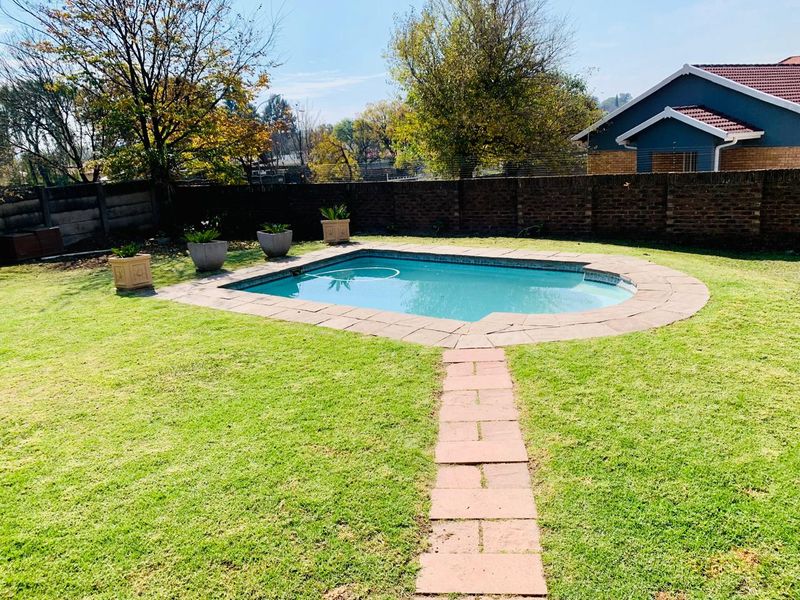 A well-maintained backyard featuring a swimming pool with a paved surround, a stone path, and a brick boundary wall.