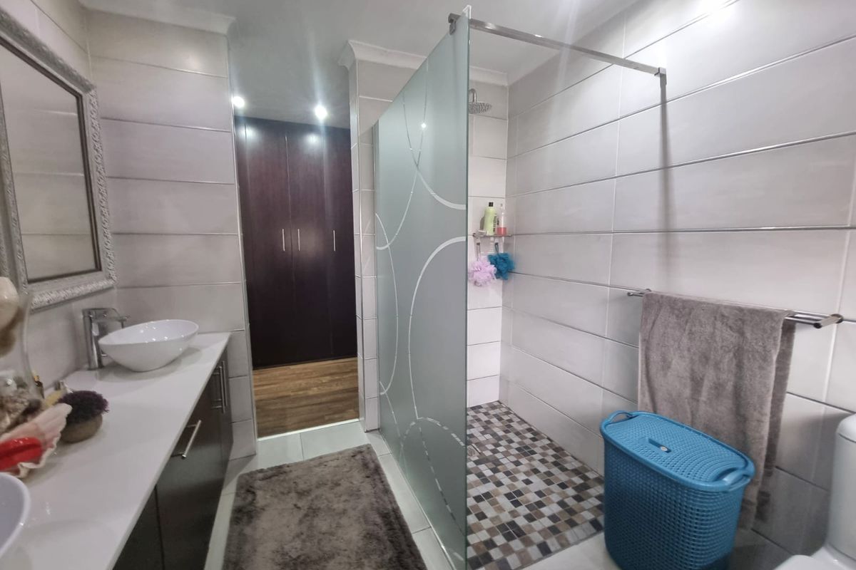 Modern bathroom featuring a walk-in shower with a frosted glass screen, a sleek vanity with a countertop basin, and ample built-in storage cupboards.