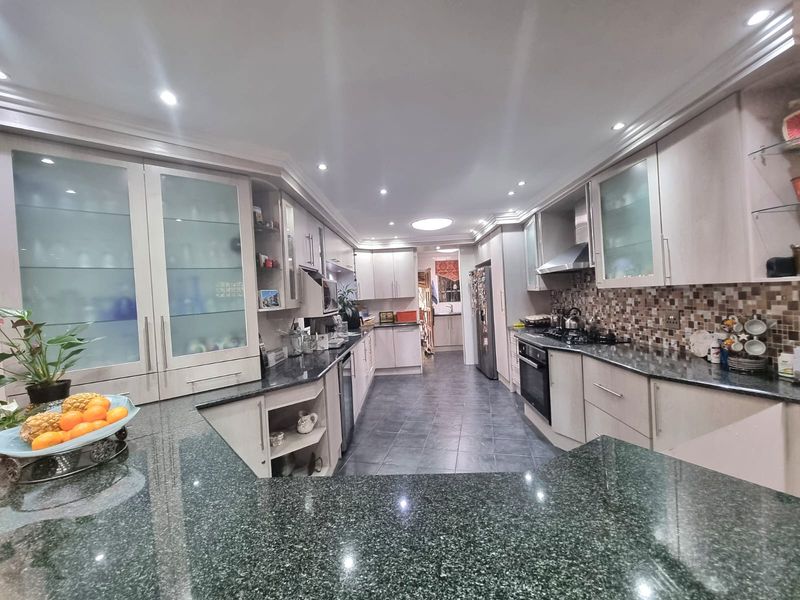 Spacious kitchen featuring granite countertops, extensive built-in cabinetry, a gas hob with extractor fan, and a mosaic tile backsplash with tiled flooring.