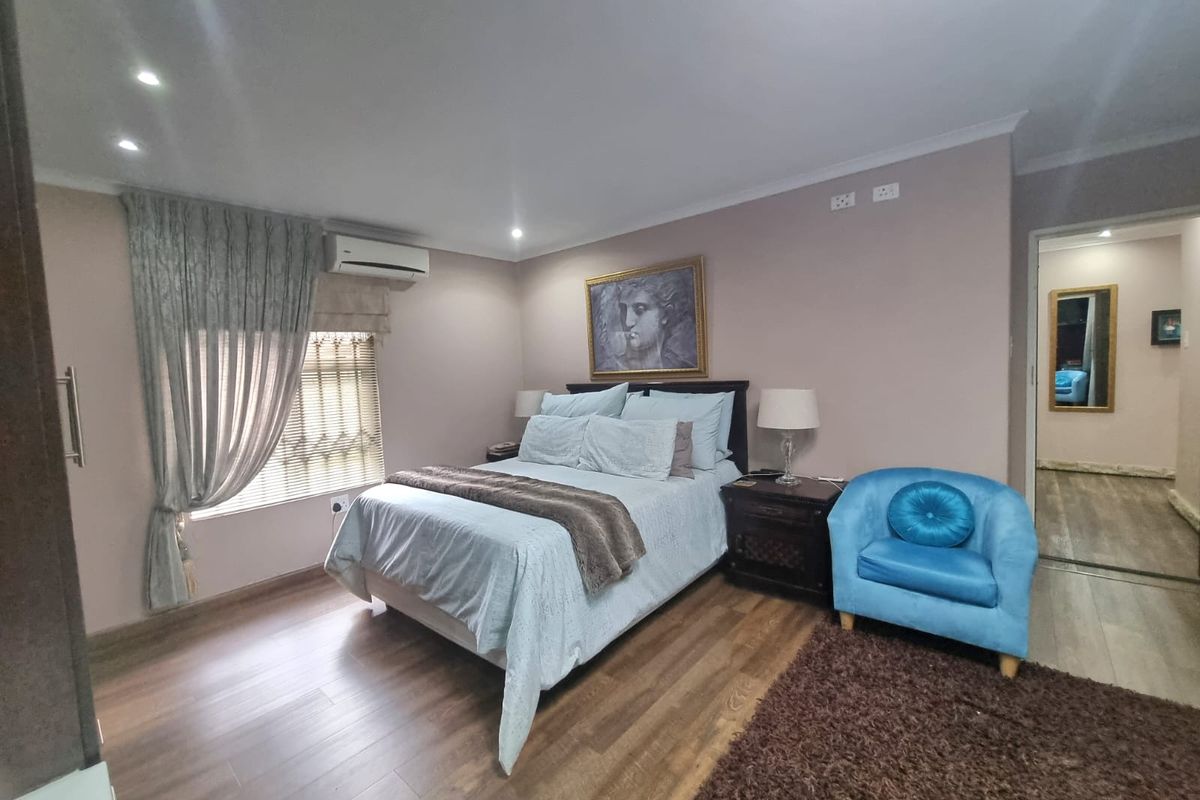 A well-maintained bedroom featuring laminate flooring, recessed downlighting, and a wall-mounted split-system air conditioning unit.