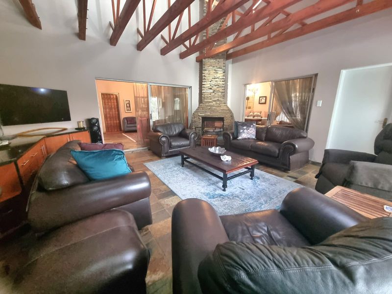 Spacious living room featuring high vaulted ceilings with exposed timber trusses, a prominent stone-clad fireplace, and durable slate tile flooring.