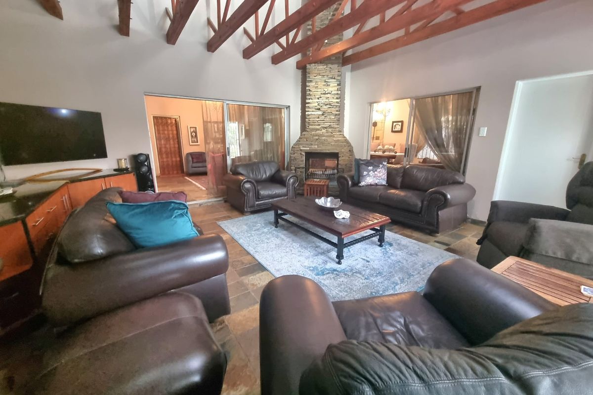Spacious living room featuring high vaulted ceilings with exposed timber trusses, a prominent stone-clad fireplace, and durable slate tile flooring.