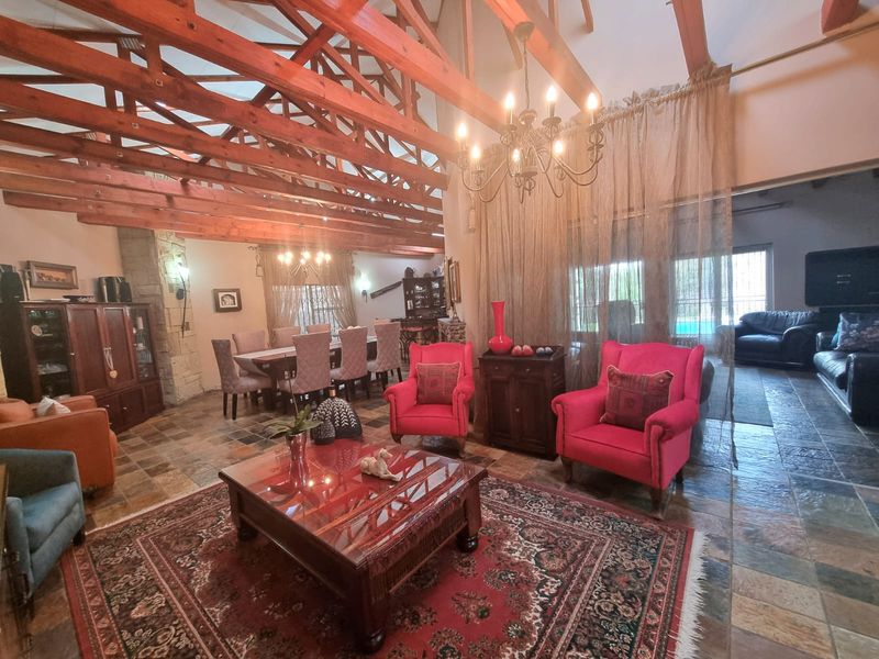 Spacious open-plan living and dining area featuring high vaulted ceilings with exposed timber trusses, slate flooring, and a rustic stone feature wall.