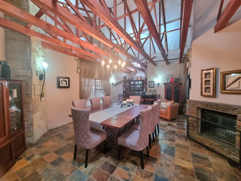 Spacious dining room featuring high vaulted ceilings with exposed timber trusses, slate tile flooring, and a prominent stone-clad fireplace.