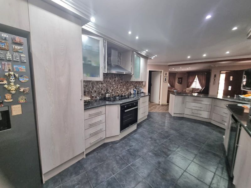 Spacious open-plan kitchen featuring light wood cabinetry, granite countertops, integrated appliances, and dark tiled flooring, flowing seamlessly into the adjacent living area.