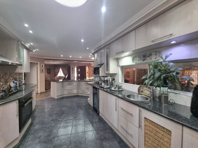 Spacious kitchen featuring light-toned cabinetry, dark granite countertops, integrated appliances, and modern recessed lighting, flowing into an open-plan living area.