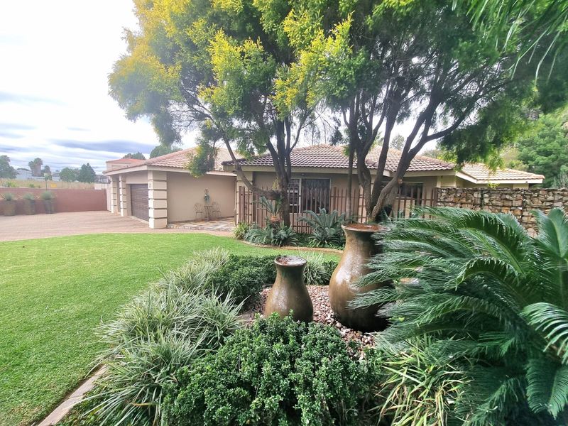 Front view of a well-maintained house featuring a landscaped garden, paved driveway, double garage, and stone retaining wall elements.