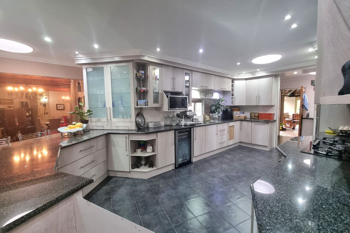 Spacious kitchen featuring extensive light-toned cabinetry, granite countertops, integrated appliances, and dark tiled flooring, offering a functional and well-lit culinary workspace.