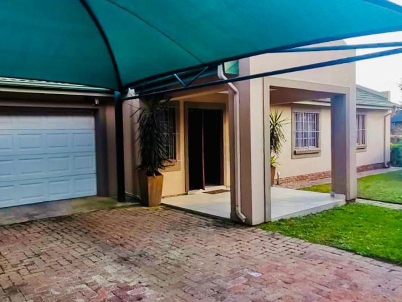 Front exterior view featuring a paved driveway, covered entrance, and a shade sail over the garage area with a well-maintained lawn.