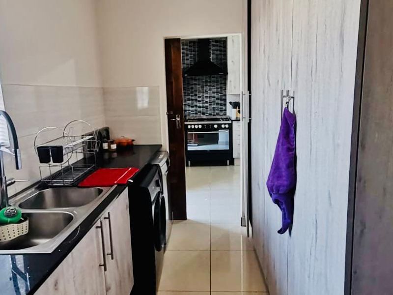 A functional scullery featuring double stainless steel sinks, modern cabinetry, and tiled flooring, with a view through to the main kitchen area.