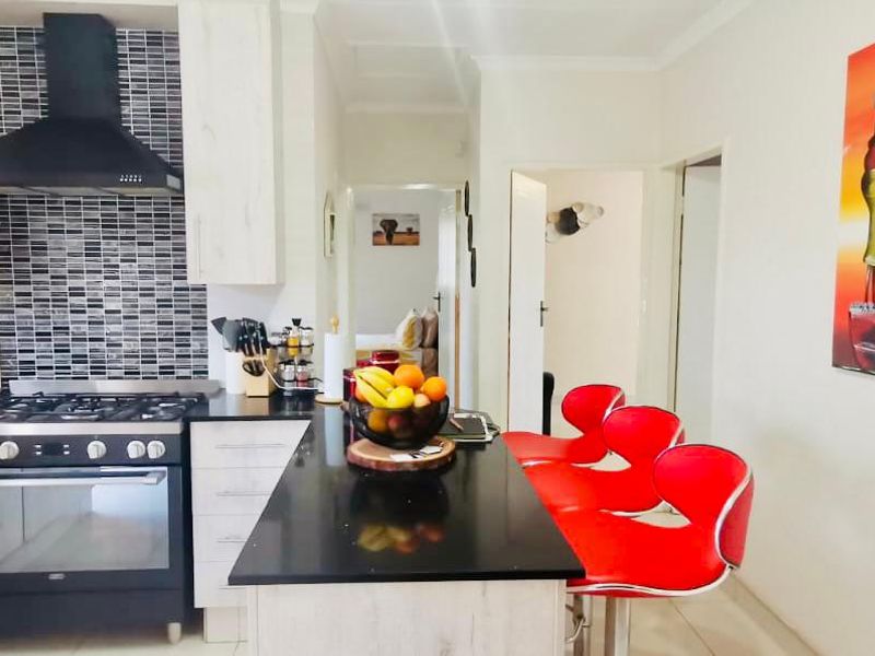 Modern kitchen featuring light wood-grain cabinetry, black granite countertops, a gas stove with extractor fan, and a stylish mosaic tile backsplash.