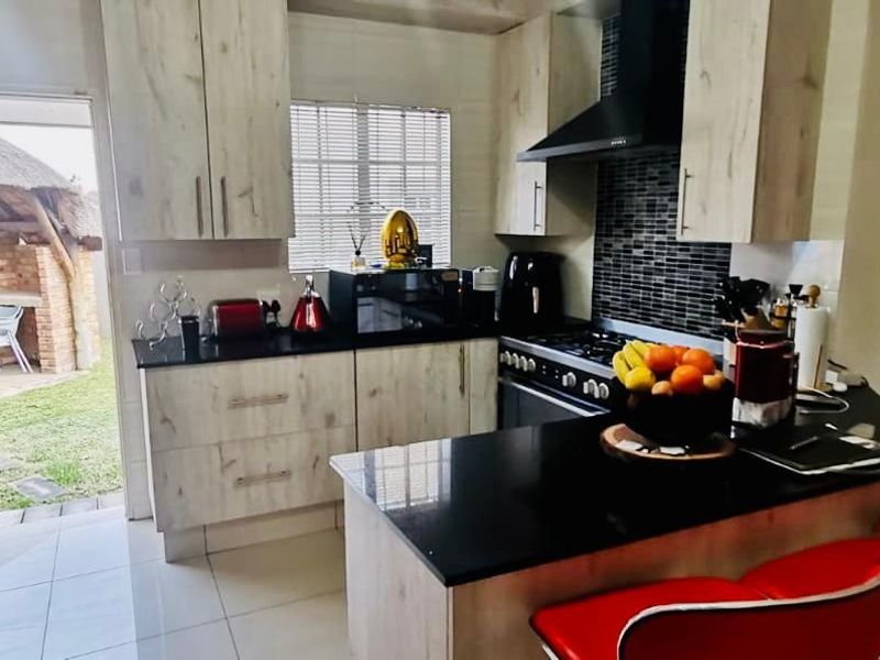Modern kitchen featuring light wood-finish cabinetry, black granite countertops, a breakfast nook, and direct access to an outdoor patio area.
