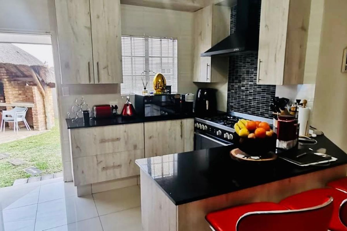 Modern kitchen featuring light wood-finish cabinetry, black granite countertops, a breakfast nook, and direct access to an outdoor patio area.