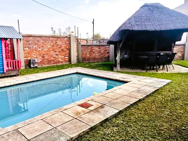 Outdoor pool area featuring a swimming pool with paved surround, a traditional thatched lapa, and secure brick boundary walls with electric fencing.