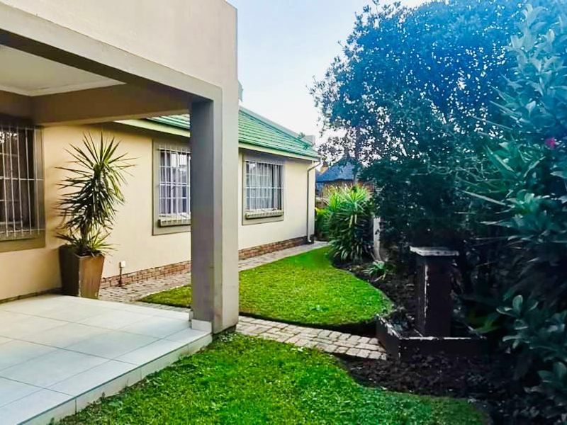 A covered tiled patio area overlooking a well-maintained garden with a brick paved pathway and established landscaping.