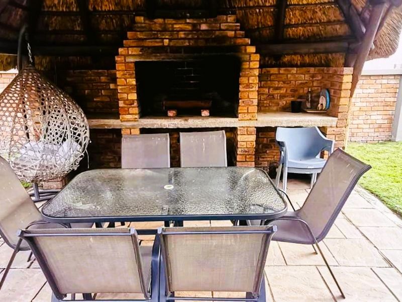 Covered outdoor patio area featuring a traditional thatched roof and a built-in brick braai, set within a private garden space.