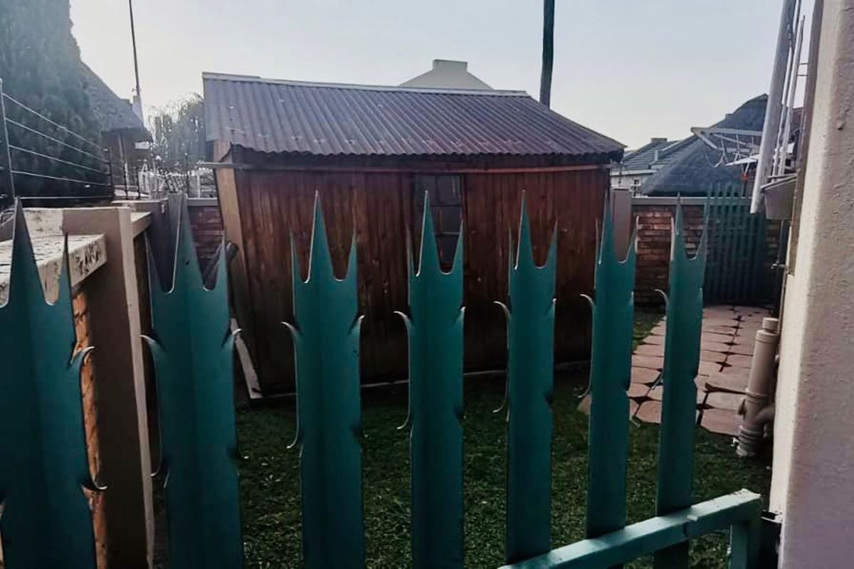 Rear garden area featuring a timber storage shed, paved pathway, and secure perimeter fencing with brick boundary walls.