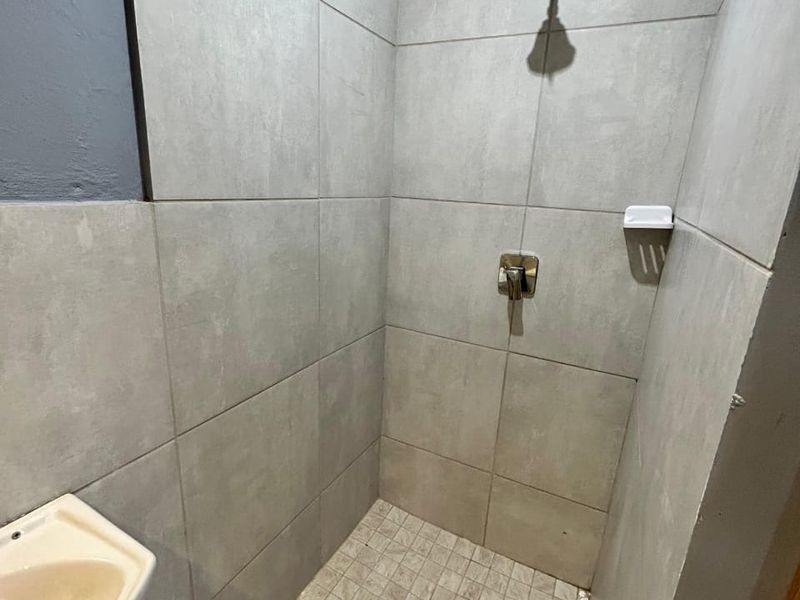 A compact shower enclosure featuring grey wall tiles, a shower mixer, and a basin, currently requiring minor repairs to the wall finish.