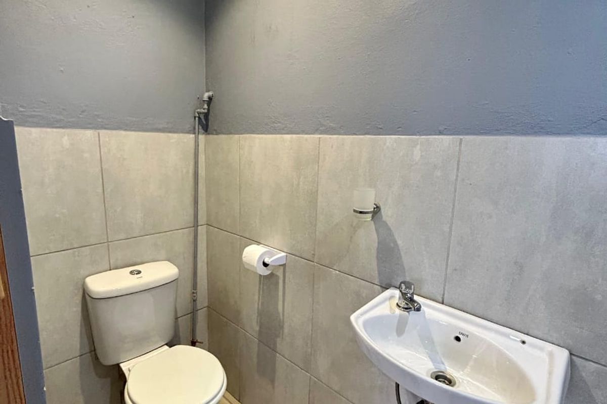 A compact guest bathroom featuring a wall-mounted basin, toilet, neutral wall tiles, and a high-level window for ventilation.