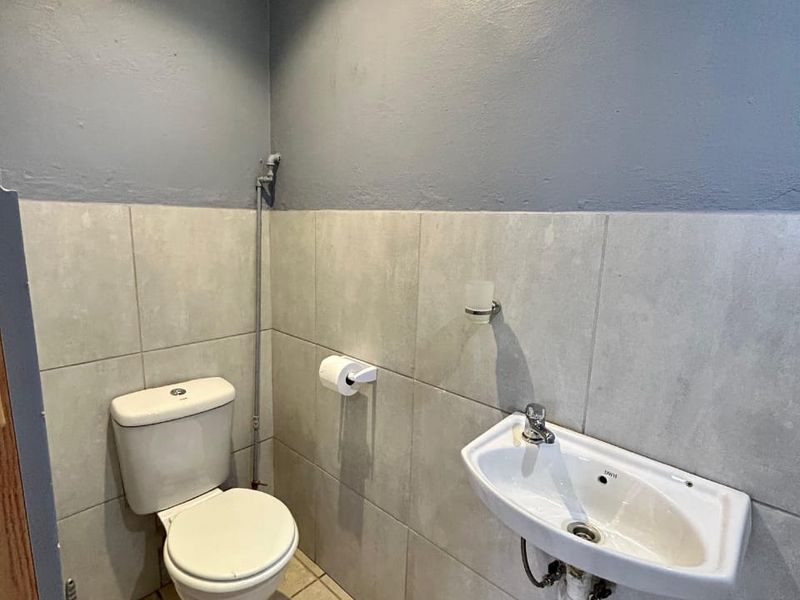 A compact guest bathroom featuring a wall-mounted basin, toilet, neutral wall tiles, and a high-level window for ventilation.