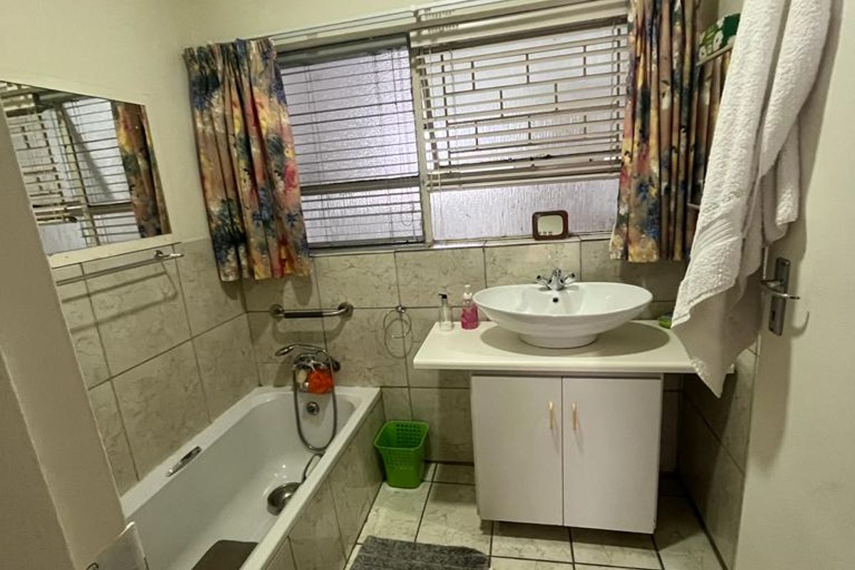 A functional bathroom featuring a built-in bathtub, a vessel sink with a vanity cabinet, and tiled finishes throughout.