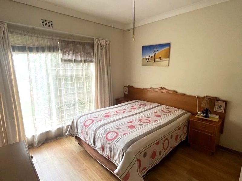 A functional bedroom featuring laminate flooring, a ceiling fan, and a sliding glass door providing natural light.